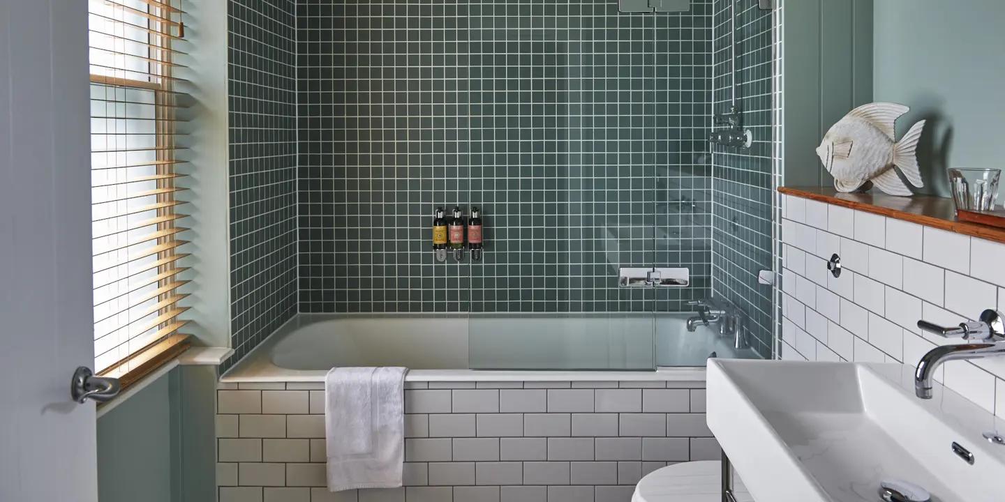 Bathroom featuring a bathtub, sink, and toilet and green tiles.