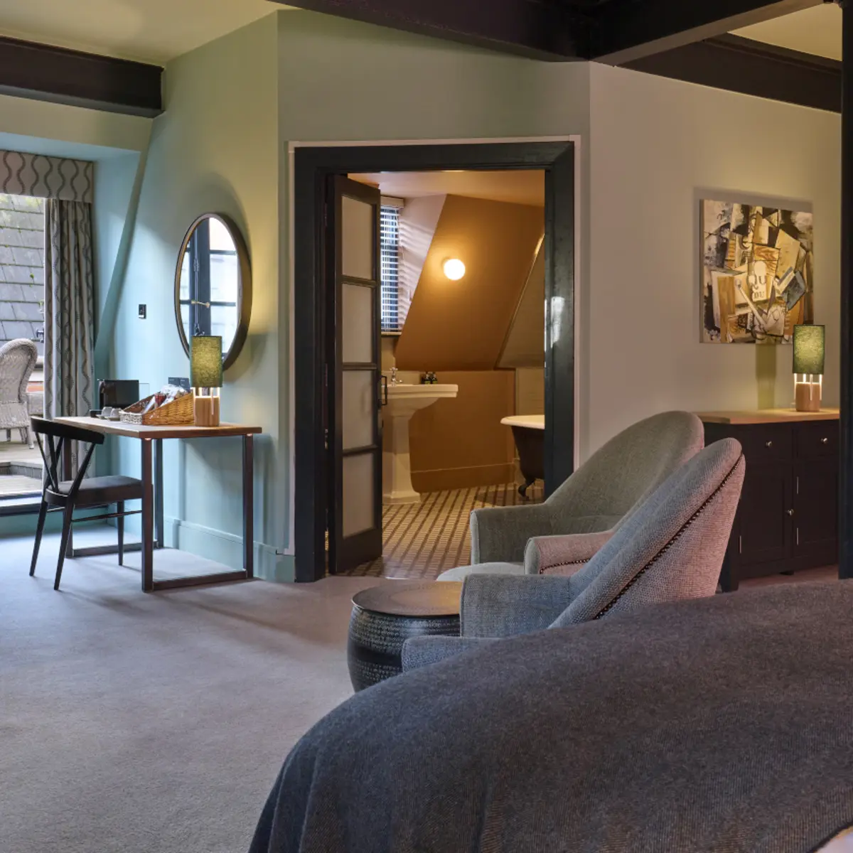 An elegantly furnished bedroom featuring a comfortable bed, stylish chair, functional desk, and modern television.