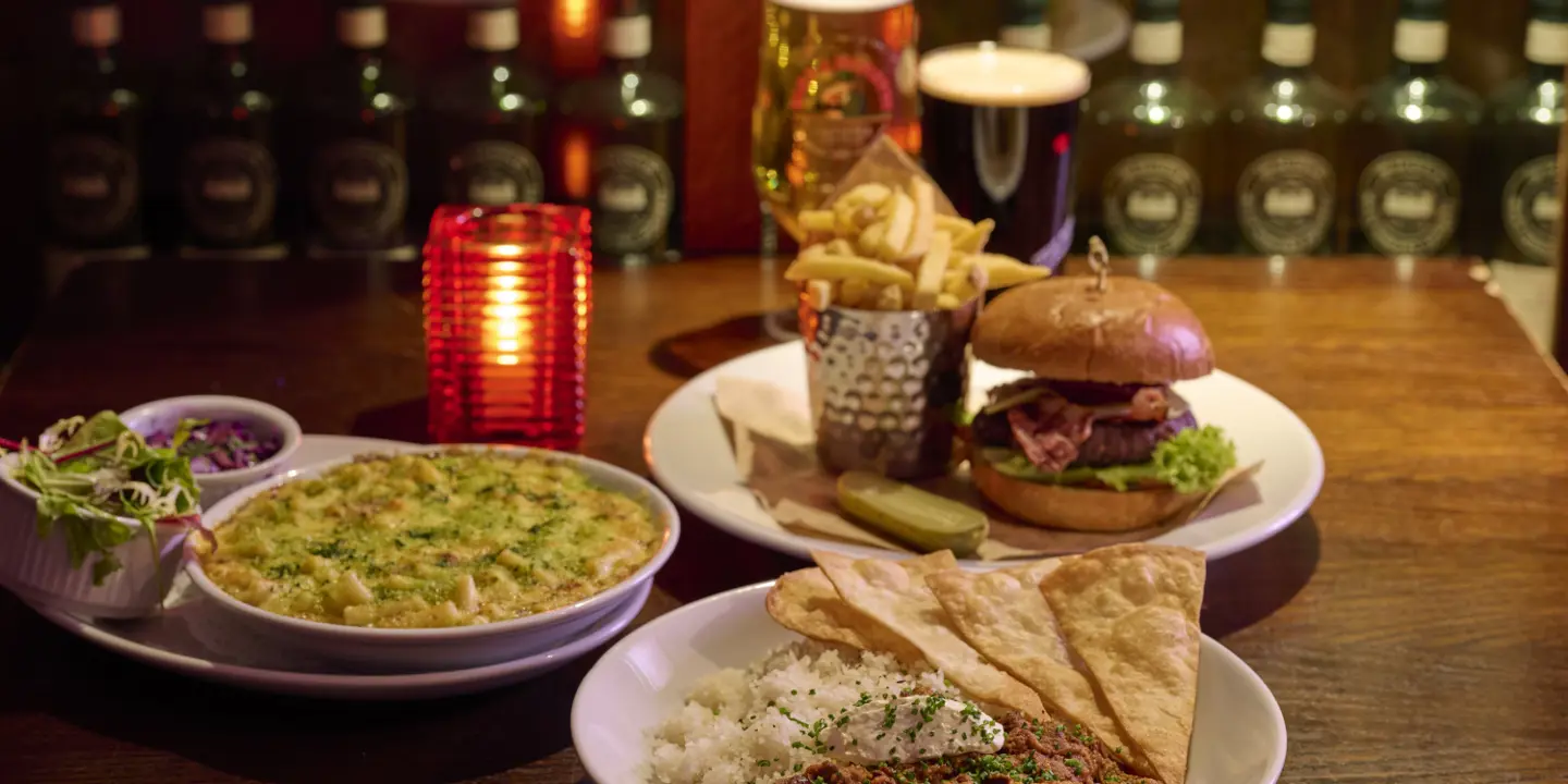 A presented meal containing 3 dishes, the 3 dishes is a burger with chips, chilli, and macaroni cheese