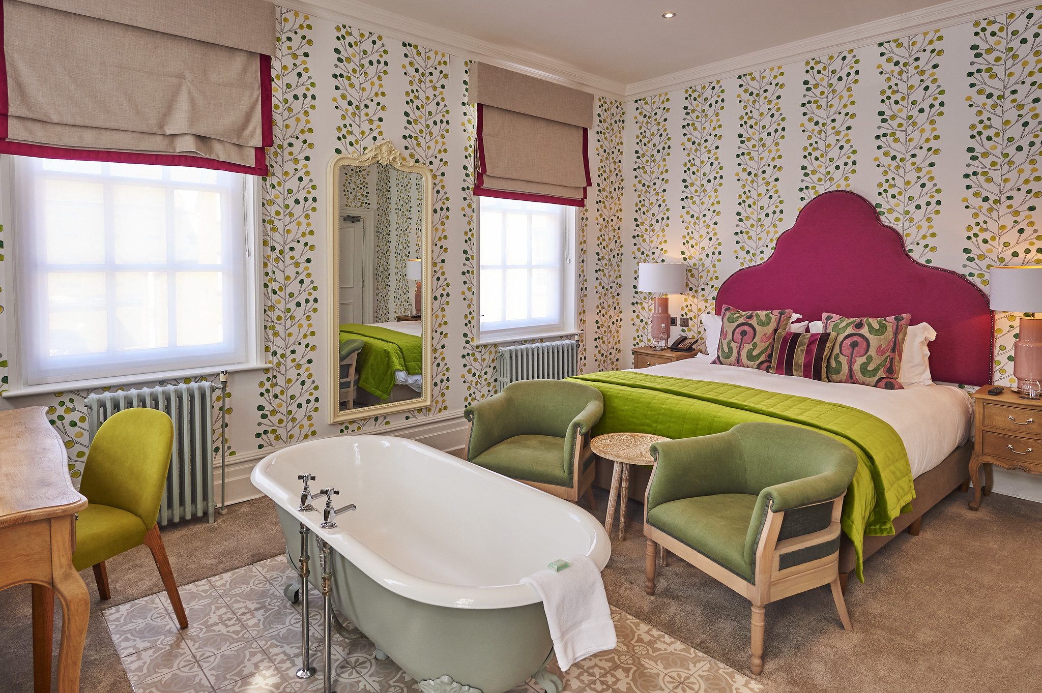 Bedroom featuring a comfortable bed, green armchairs and bathtub.