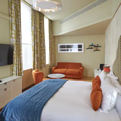 An elegantly furnished hotel room featuring a comfortable bed, plush couch, and modern television.