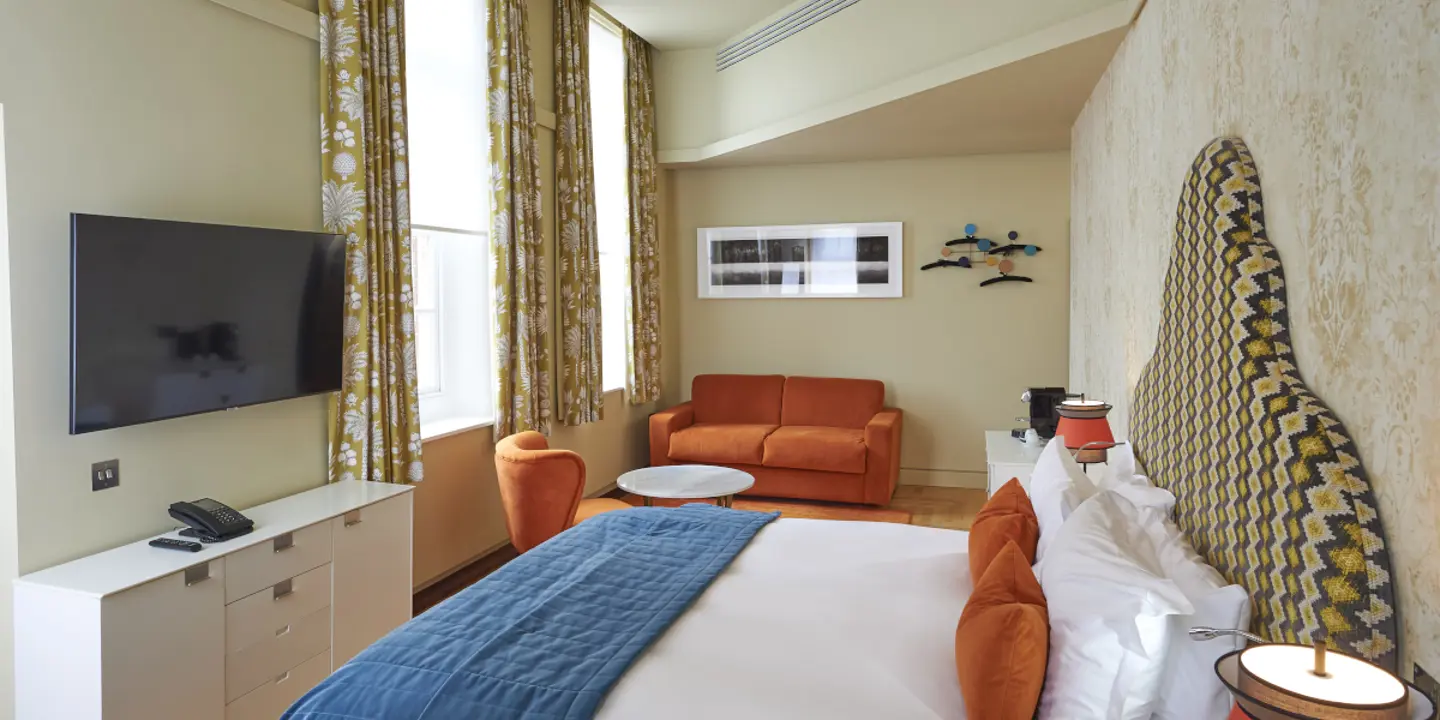 An elegantly furnished hotel room featuring a comfortable bed, plush couch, and modern television.