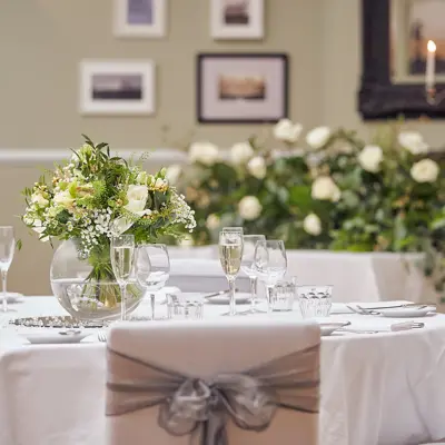 Round table adorned with white cloth, champagne glasses and flower arrangements.