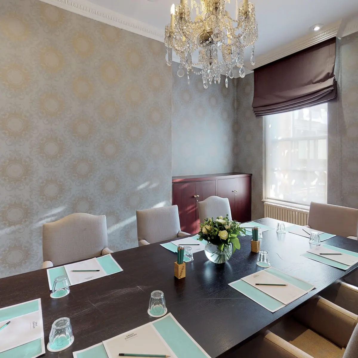 A dining room featuring a long table, chairs, and an elegant chandelier.