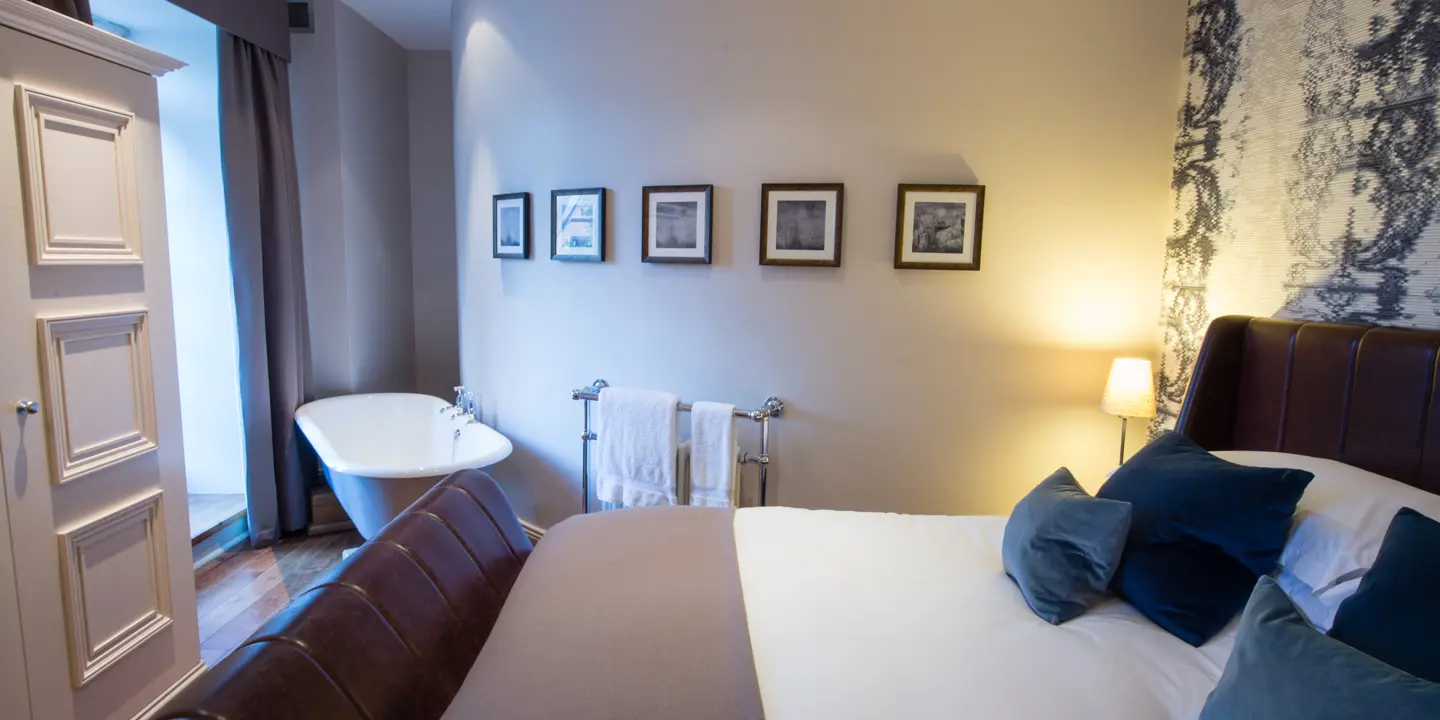 A bed that's adjacent to the wardrobe with a bath positioned by the window