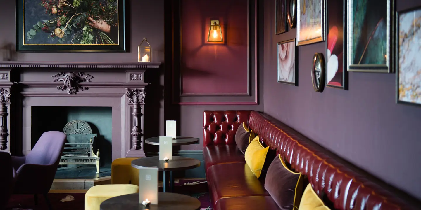 A dark red leather sofa, dark tables and yellow stools, next to a cozy fireplace.