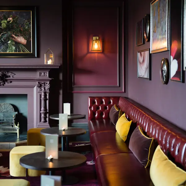 A dark red leather sofa, dark tables and yellow stools, next to a cozy fireplace.