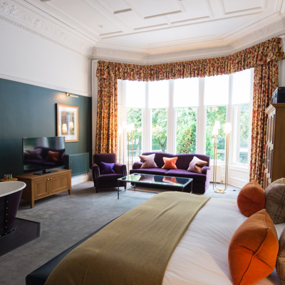 An elegantly furnished hotel room featuring a comfortable bed, plush couch, and modern television.