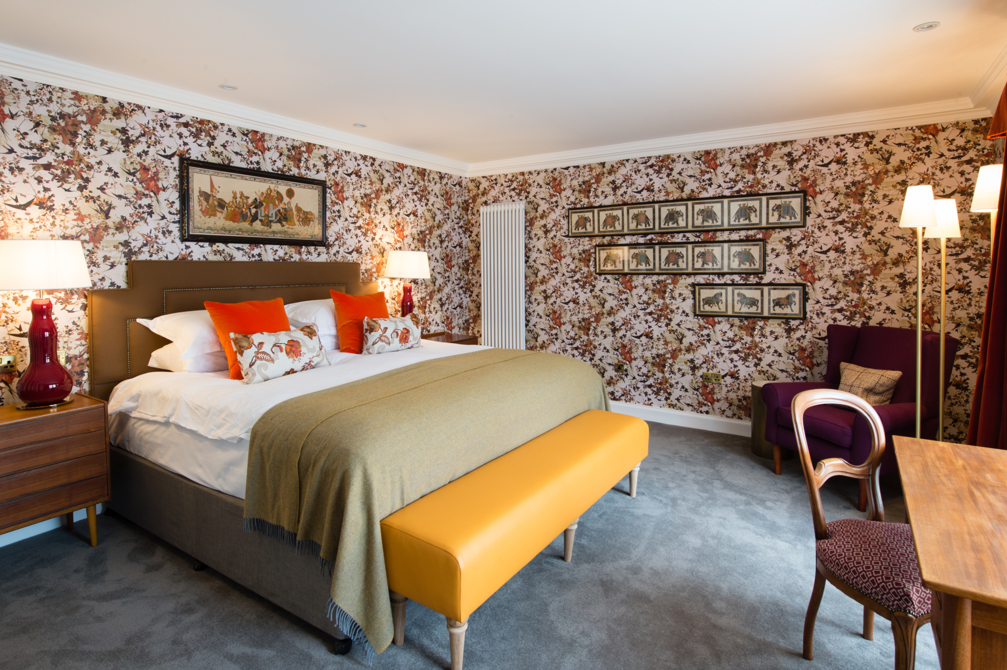 An elegantly furnished bedroom featuring a comfortable bed, a stylish chair, a sleek table, and captivating artwork adorning the walls.