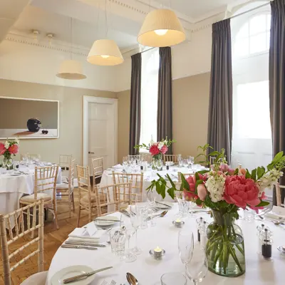 Multiple tables arranged for a formal dinner with a vase of flowers.