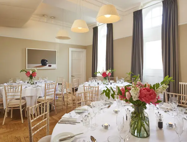 Multiple tables arranged for a formal dinner with a vase of flowers.