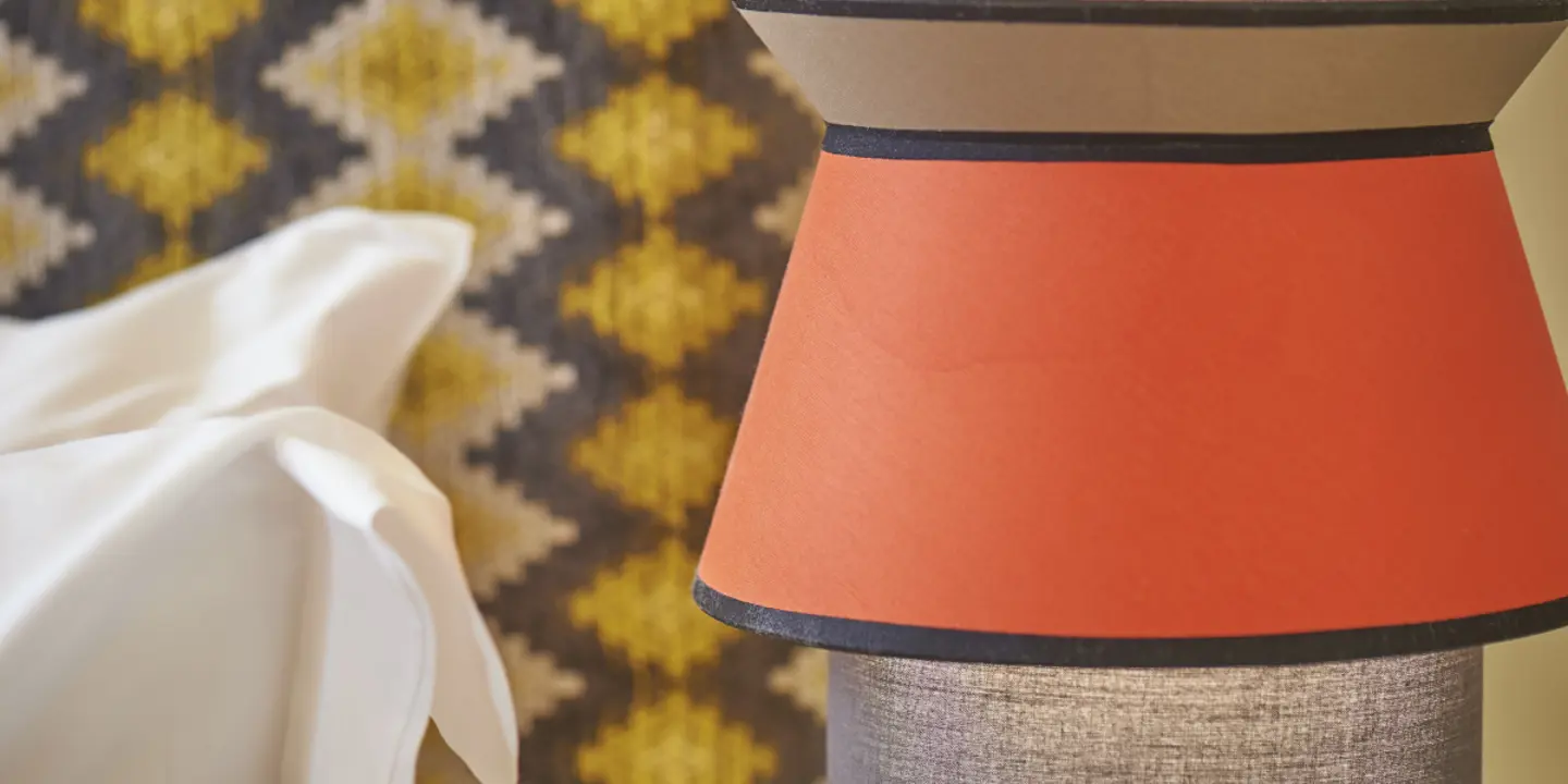 A close-up view of a pillow resting on a bed and orange lamp shade.