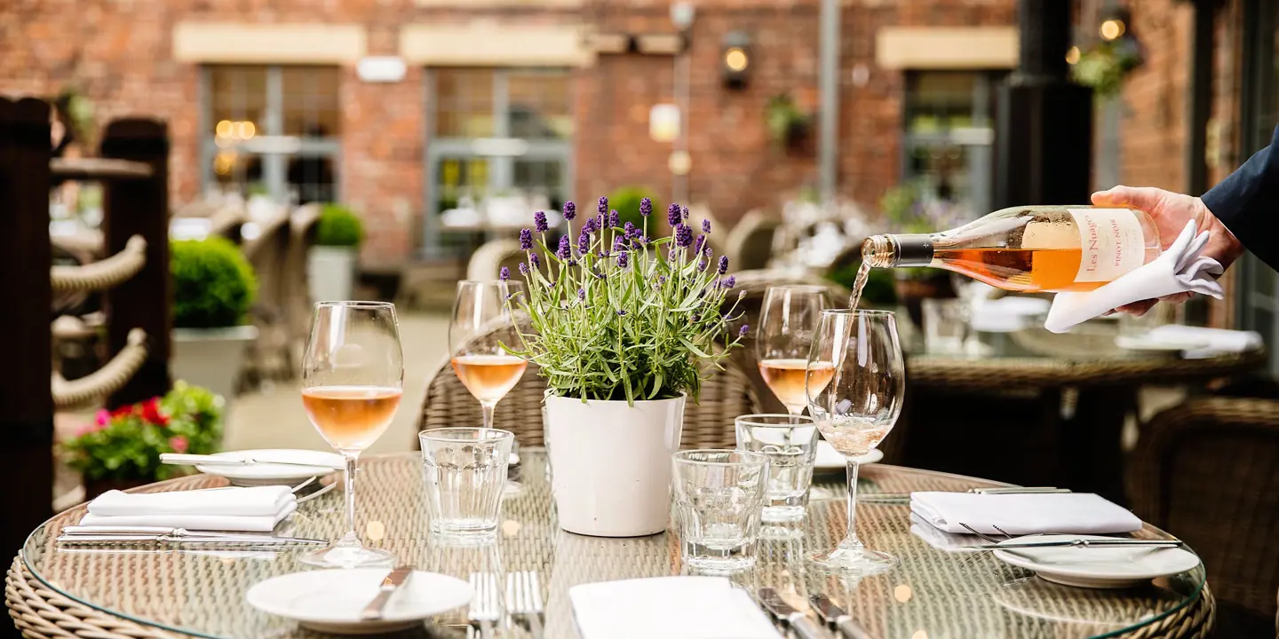A person pouring wine into a glass on a table.