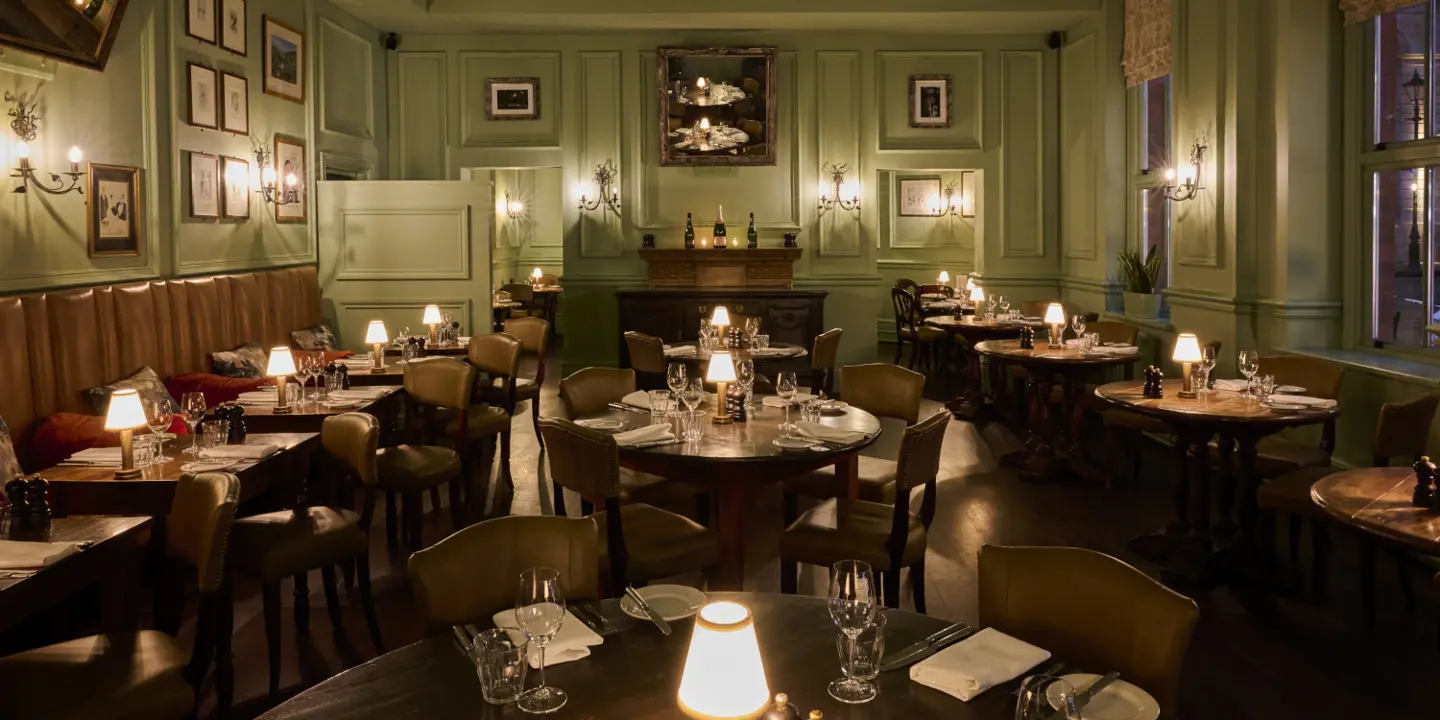 A prepared lowly lit dining hall with wooden tables and chairs