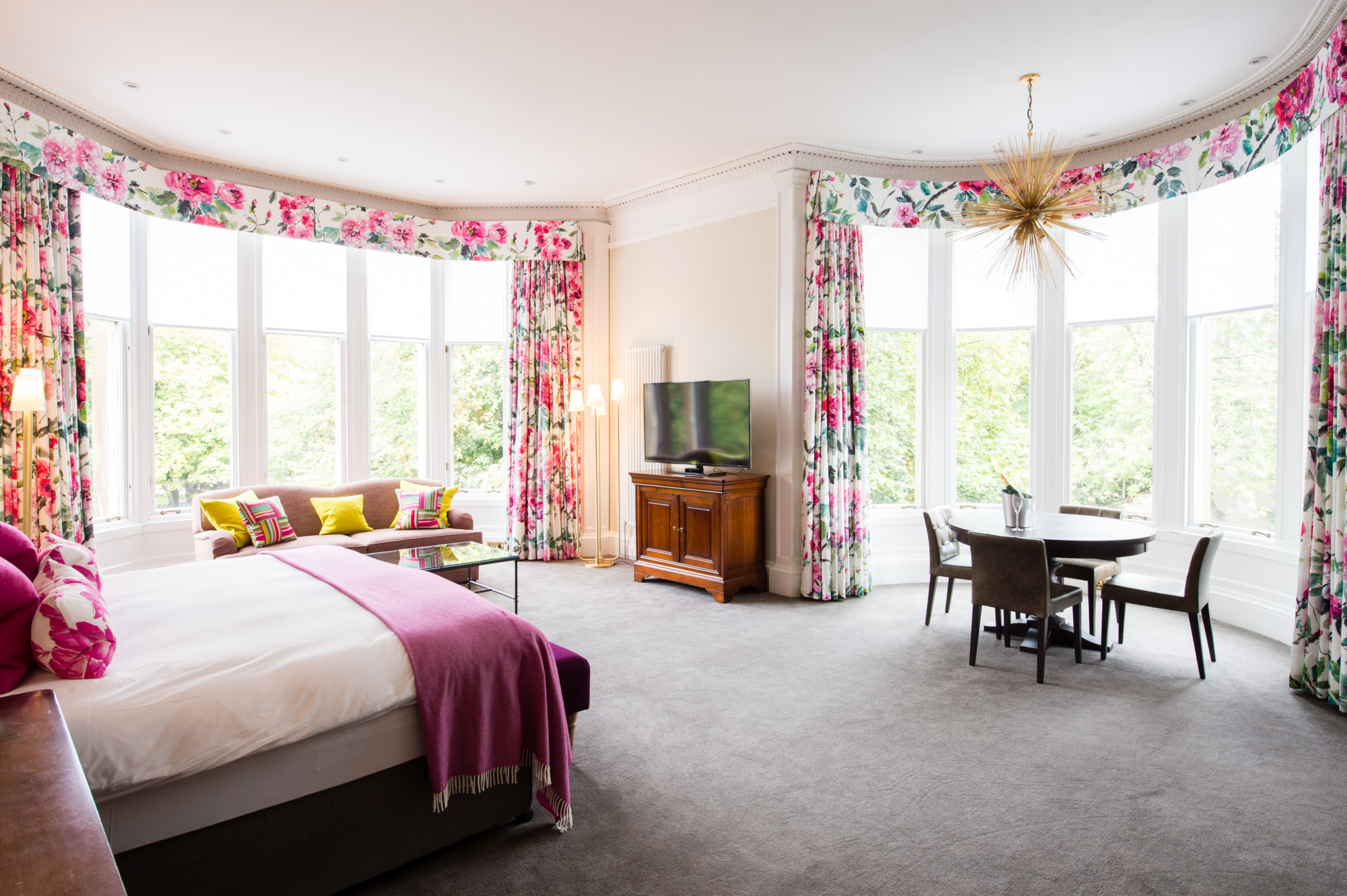 An elegantly furnished bedroom featuring a comfortable bed, stylish chair, sleek table, and modern television.