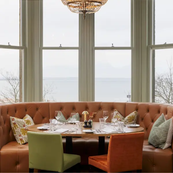 A beautifully arranged table with elegant wine glasses and neatly set place settings, placed in front of a picturesque bay window.