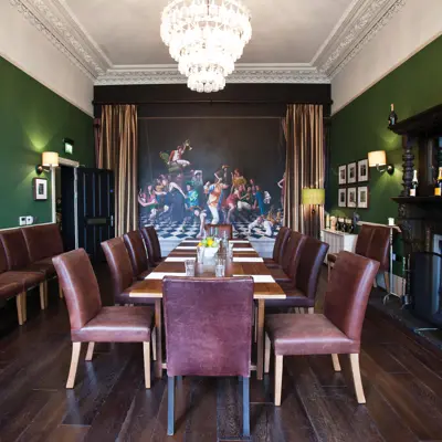 A long wooden table adorned with a bowl of fresh fruit. There are extra chairs in the room