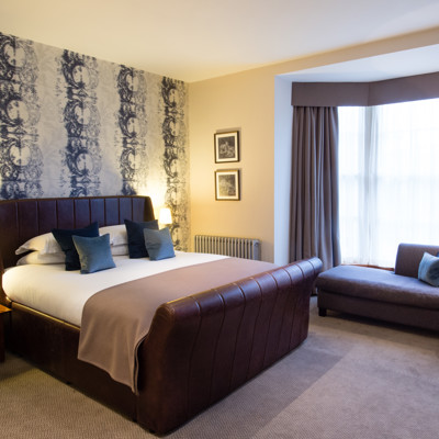 Elegantly made brown leather bed, with plump pillows and 2 framed pictures on the wall