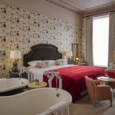 A room containing a double bed, 2 chairs, a table, and 2 bathtubs