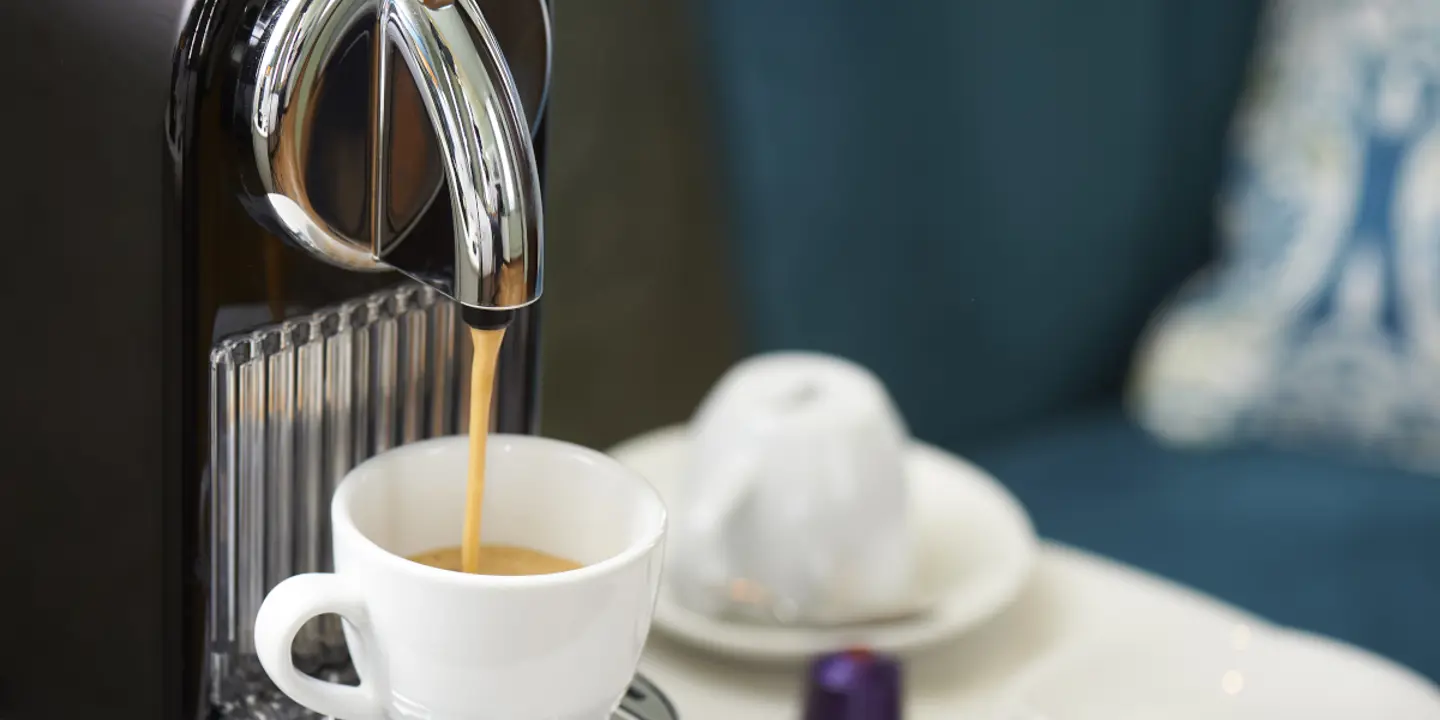 A cup of coffee being poured by a coffee machine.