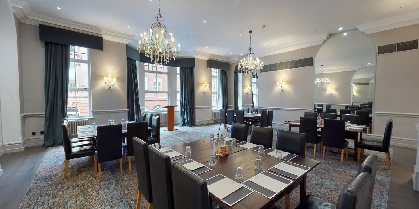 A selection of tables and chairs in a meeting room with 2 elegant chandeliers.