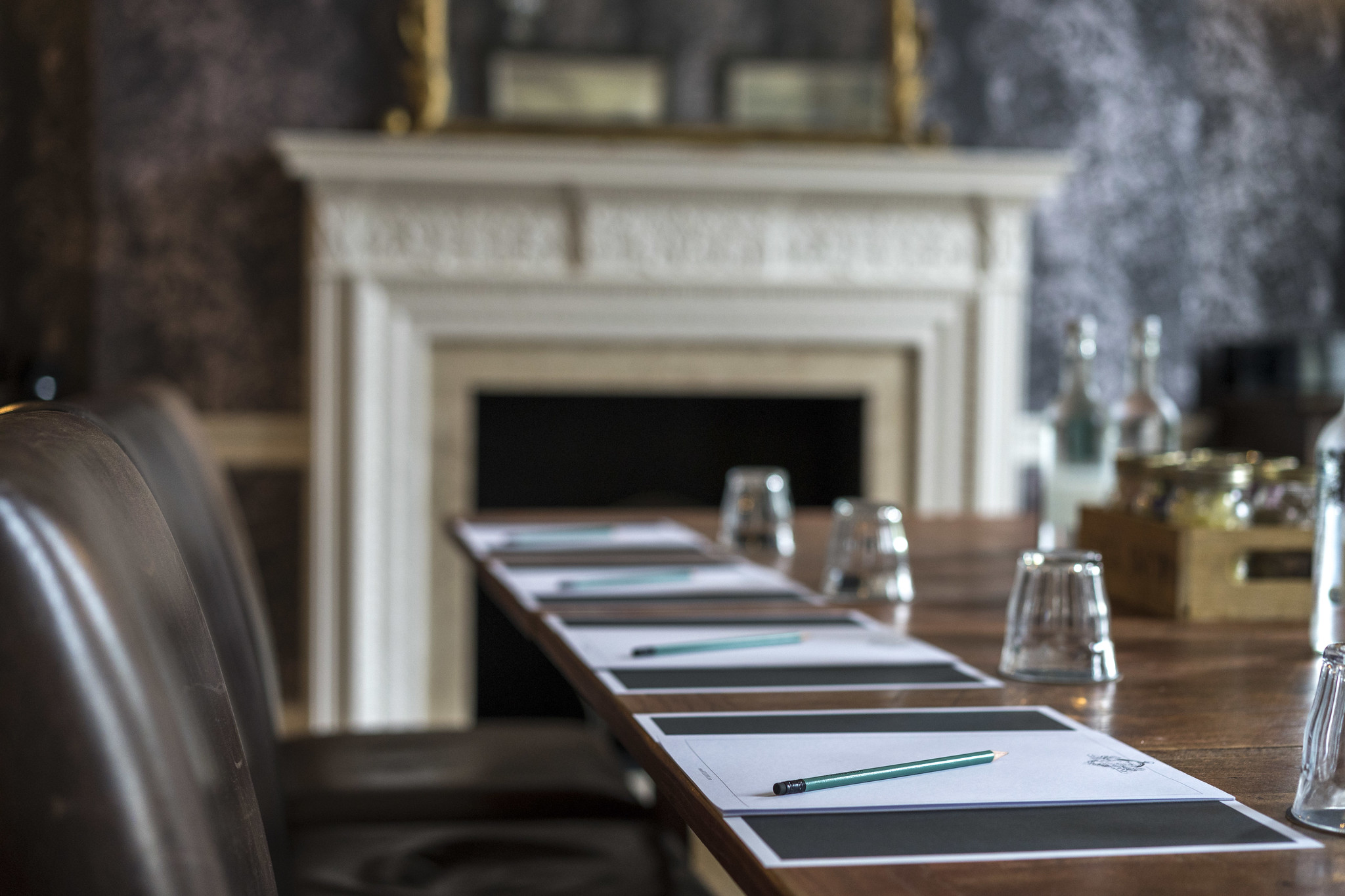 A close up of a wooden meeting room table, there is pen, paper, and empty water glasses visible 